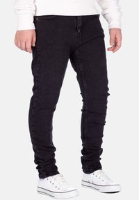 Jeans skinny neri in denim con una texture strappata, caratterizzati da un classico design a cinque tasche e abbinati a sneakers bianche basse.