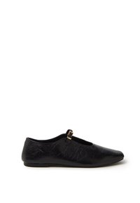 Zapato de cuero negro con un acabado suave, punta redondeada, suela plana y una pequeña correa con una hebilla dorada.