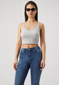 Top corto de canalé gris con tirantes ajustables, combinado con unos vaqueros de tiro alto en azul oscuro con detalles desgastados. Gafas de sol negras.