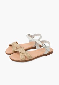 Białe sandały z krzyżującymi się plecionymi paskami z naturalnych włókien, z brązową podeszwą i zapięciem na klamrę na pasku wokół kostki.