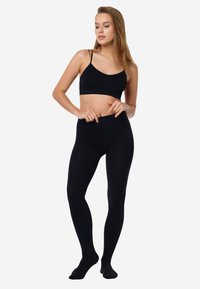 Leggings neri e elasticizzati caratterizzati da un alto punto vita. La modella indossa anche un bralette nero abbinato. Entrambi gli articoli sono morbidi e aderenti.