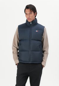 Navy puffer vest with a high collar, front zipper, and logo detail. Features quilted sections for insulation and a lightweight design.