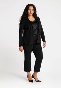 Svart kavaj med prickig textur, ihop med en svart satinblus och korta svarta byxor. Bärs med spetsiga svarta klackar.