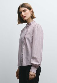 Striped blouse in light pink and white, featuring a high collar, ruffled front placket, and long, gathered sleeves. Smooth fabric texture.