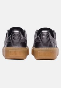 Baskets en cuir noir avec une semelle en gomme plate, présentant une finition texturée et un logo Puma bien visible sur le talon et l'arrière.