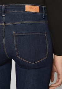 Mörkblå denimjeans med midjehöjd, bakfickor med kontrasterande sömmar och en läderetikett märkt "ONLY."