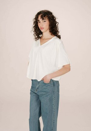T-shirt blanc à col en V avec des manches courtes, coupe décontractée et texture douce, associé à un jean en denim bleu clair à taille haute.