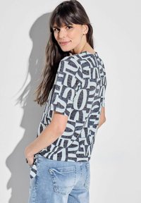 Kortærmet skjorte i lys blå med et dristigt sort teksttryk, med rund halsudskæring og afslappet pasform, parret med lyse denimjeans.