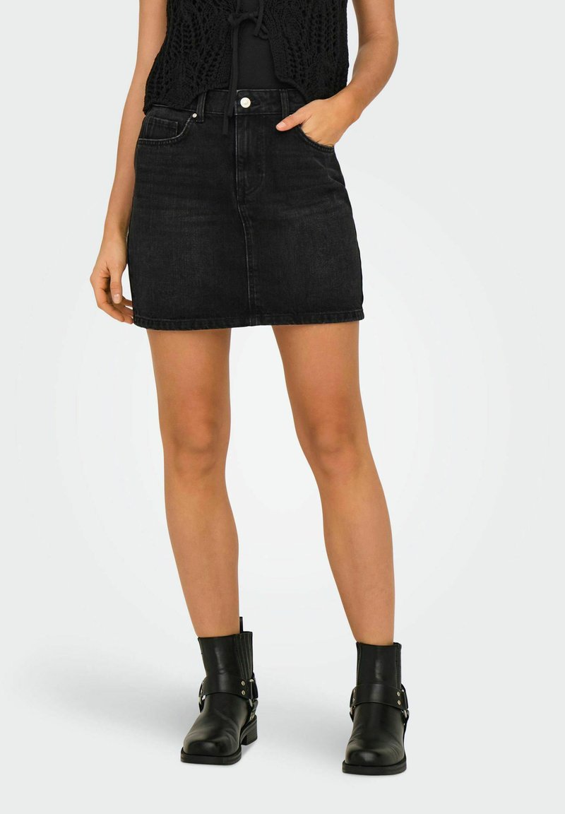Zwarte denim mini-rok met een getailleerde pasvorm, vijf zakken en een rauwe zoom. Gecombineerd met zwarte enkellaarzen met een gesp-accent.