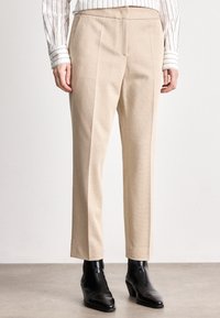 Calças beige ajustadas com um tecido texturizado, corte reto e costuras laterais. Combinadas com botas de tornozelo pretas.