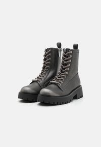 Bottines de combat grises à lacets avec une semelle épaisse noire, texture lisse et détail de fermeture éclair. Présente des œillets renforcés et une languette à l'arrière.