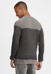 Strikkegenser med teksturert design, med en gradient av mørkegrå og lysegrå farger. Ribbestrikkede mansjetter og fald. Rund hals.