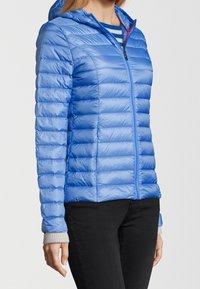 Blå puffy-jacka med huva, med horisontell quiltad stoppning, en framzipper och kontrasterande röda detaljer. Ärmarna är ljusgrå.