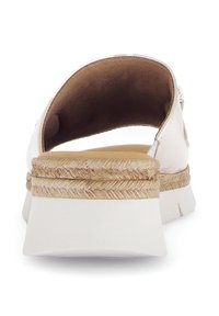 Bílé sandály s tlustou platformou, které mají kolem podrážky tkaný jutový akcent a hladký, zakřivený svršek. Otevřený design na zadní straně.