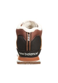 Brun textilöverdel med svarta accenter, vit logotyp och tanfärgad sula. Har en mjuk, pälsfodrad krage och svarta randdetaljer.