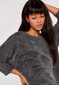 Übergroßer schwarz-weißer Pullover mit einem wellenförmigen Muster, rundem Ausschnitt und Dreiviertelärmeln aus strukturiertem Stoff.