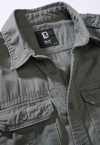 Olívazöld ing gombos elülső résszel, két mellzsebbel és kitágított gallérral. Masszív anyagból készült, tónusos varrással. A márkajelzés látható.