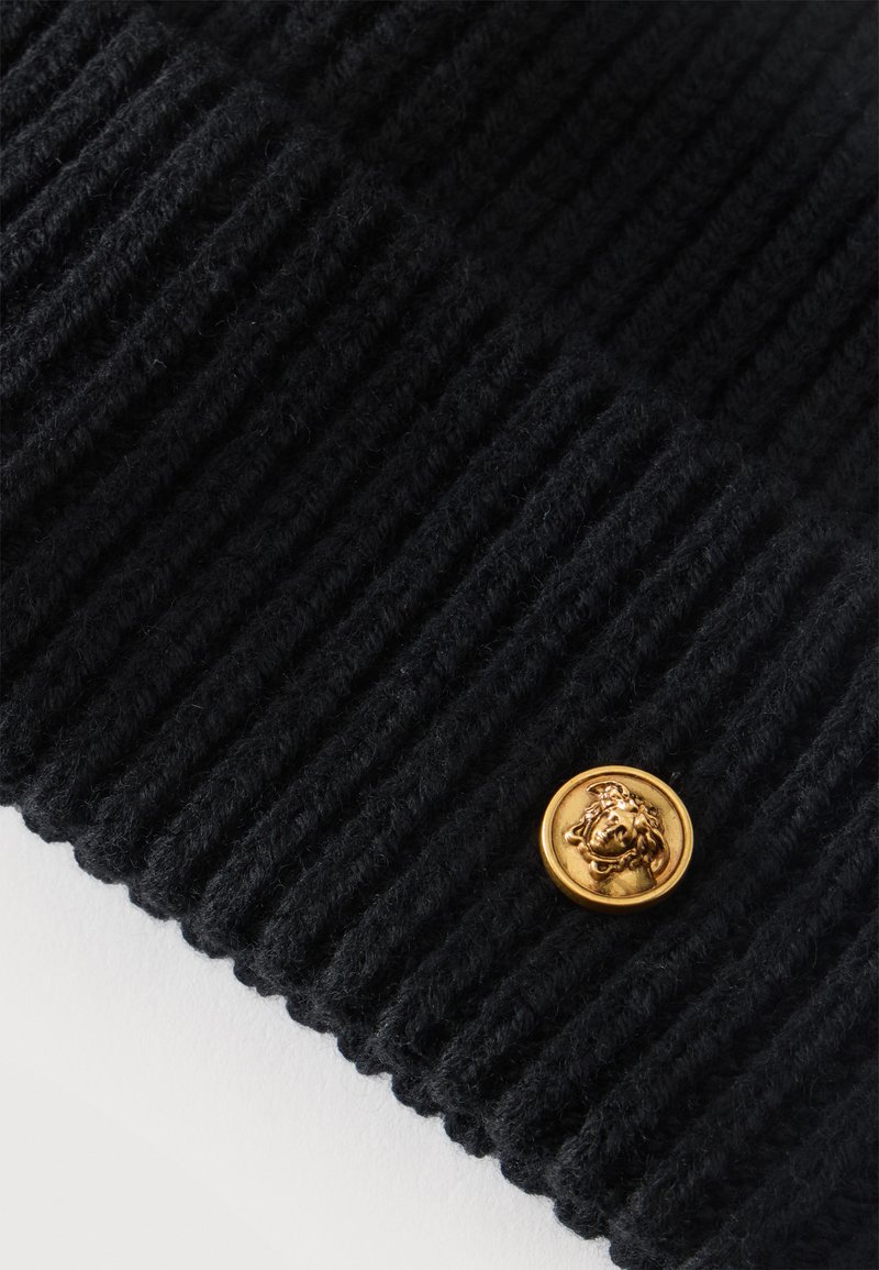 Black ribbed knit fabric with a small round gold button featuring a raised lion head design near the edge.