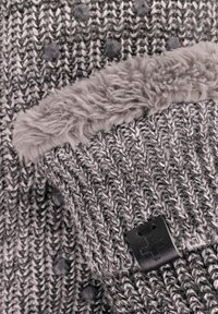 Grau gestrickte Mütze mit umschlagbarem Rand, weicher Fellfütterung und kleinen strukturierten Pom-Pom-Details, mit einem angenähten schwarzen Lederetikett.