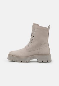 Beige Wildleder-Ankle Boots mit runder Zehenform, Schnürung vorne und einer stabilen, strukturierten Gummisohle. Mit Kontraststichen und einer Schlaufe zum Hineinschlüpfen hinten.