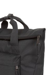 Black backpack with a textured fabric, top handle, zip closure, and small exterior pocket with metallic hardware.