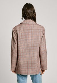 Blazer de cuadros en marrón y beige con sutiles acentos rojos. Hombros estructurados, solapa muestrariada y una abertura en la parte trasera. Corte casual.