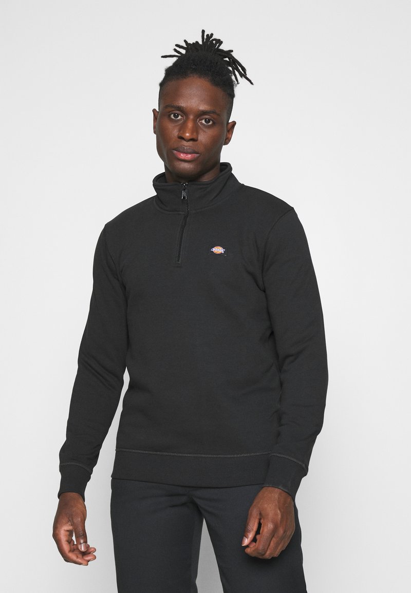 Black zip-up sweatshirt with a high collar, made of soft fabric, featuring a small logo on the chest and ribbed cuffs and hem.