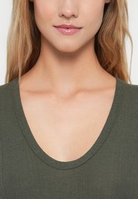 Olijfgroen geribbeld topje met een diepe V-hals, met een gladde textuur en naadloze randen rond de halslijn en schouders.