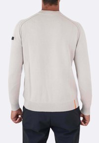 Maglione a maglia grigio chiaro con polsini e orlo a costine. Presenta un accento arancione a contrasto sul lato inferiore e una toppa con logo nero sulla manica.