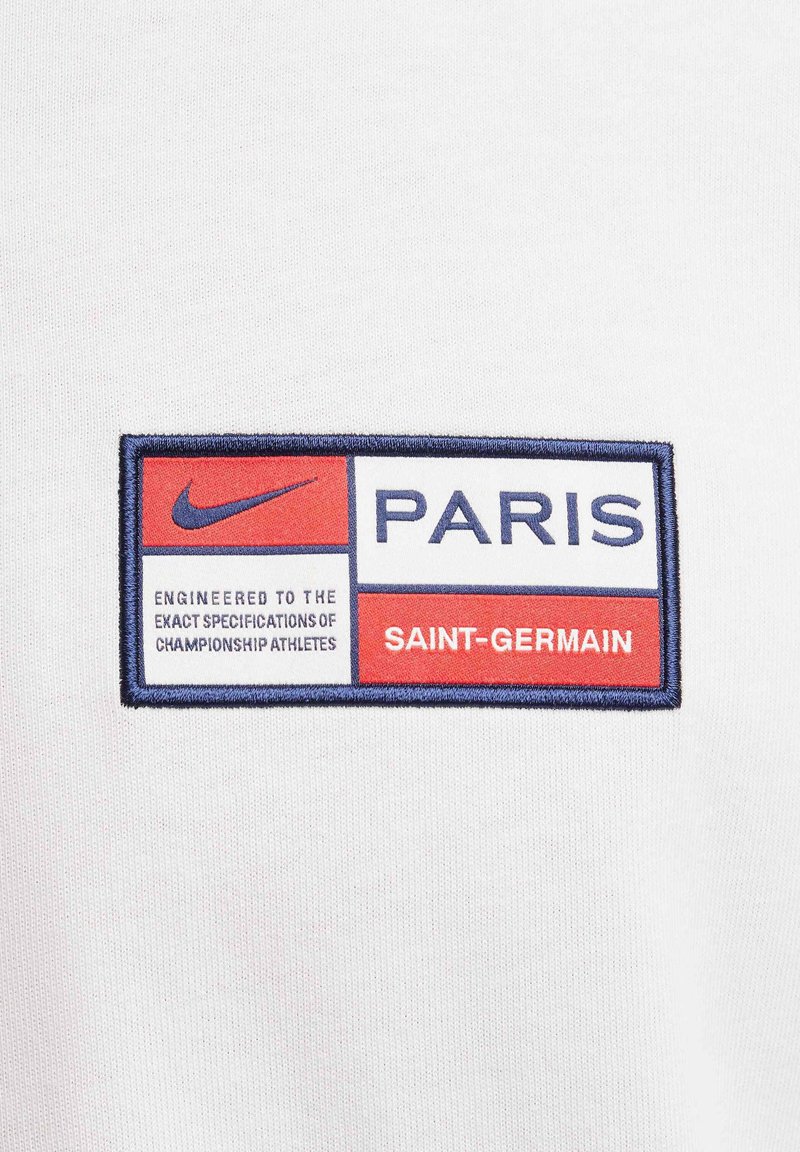 Logo Nike na białej łatce materiałowej. Ma czerwono-niebieską kolorystykę. Tekst brzmi „PARYŻ” i „SAINT-GERMAIN” z dopiskiem „Opracowane zgodnie z dokładnymi specyfikacjami...”