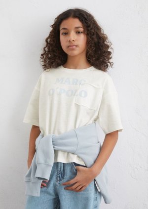 Kurzärmliges, hellcremefarbenes T-Shirt mit blauer "MARC O’POLO"-Schrift und einer linken Brusttasche, kombiniert mit einem hellblauen Sweatshirt, das um die Taille gebunden ist.