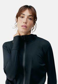 Maglia nera da atletica con zip realizzata in materiale liscio e leggero, con maniche lunghe e colletto alto, caratterizzata da un design minimalista e dettagli di cucitura.