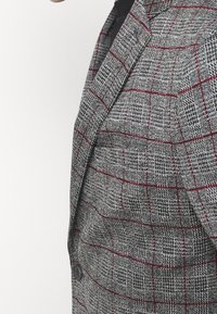Grijze blazer met een hertenstaartpatroon en rode accenten; enkele knoopsluiting, notch lapel en textuurstof.