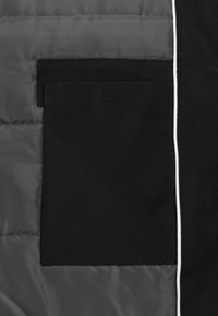 Schwarzer Außenstoff mit glatter Textur, ausgestattet mit einer rechteckigen Tasche. Kontrastierendes graues Futter und weiße Paspelierungen entlang der Kante.