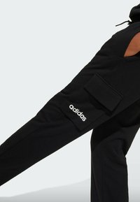 Svarta träningsbyxor med en sidoficka i cargo-stil och vit "adidas"-logotyp. Tillverkade av mjukt material, med en avsmalnande ben-design.
