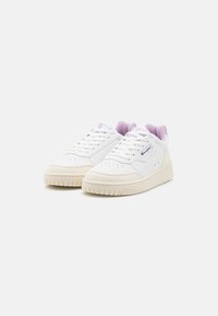 Sneakers bianchi con una tomaia in pelle liscia, dettagli lilla chiaro sulla linguetta e una suola in gomma crema testurizzata. Presentano perforazioni sulla punta.