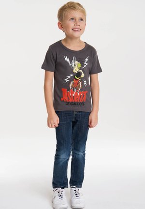 Camiseta de algodón gris con un gráfico colorido de Astérix y rayos, combinada con jeans azul oscuro y zapatillas blancas.