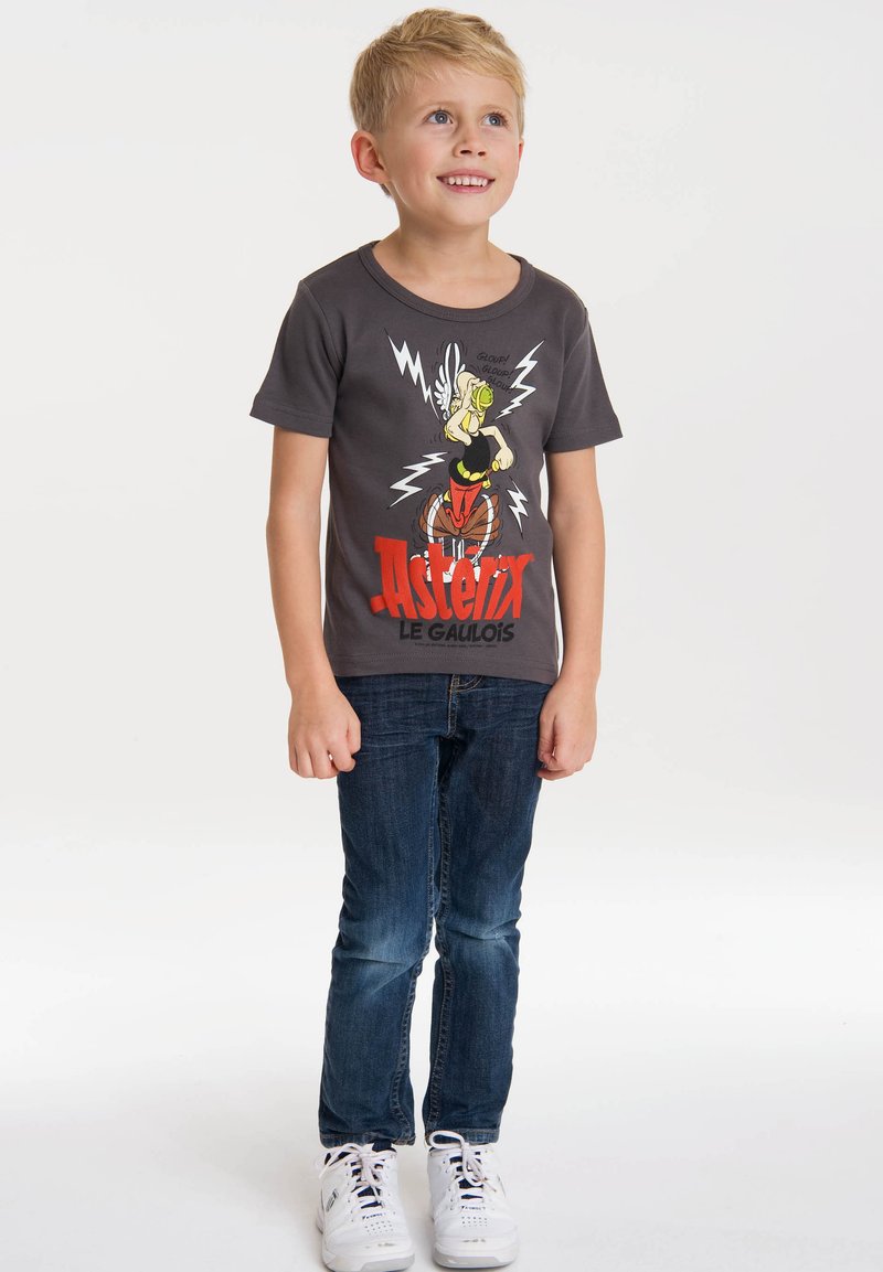 T-shirt in cotone grigia con una grafica colorata di Asterix e fulmini, abbinata a jeans blu scuro e sneakers bianche.
