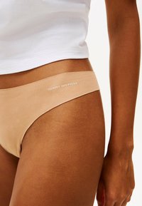 Perizoma beige Tommy Hilfiger realizzato in tessuto morbido, con una cintura morbida e il nome del marchio stampato in bianco.