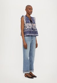 Top con estampado floral y acentos en azul marino, con mangas rizadas y lazo ajustable. Combinado con jeans rectos de color azul claro y zapatos planos oscuros.