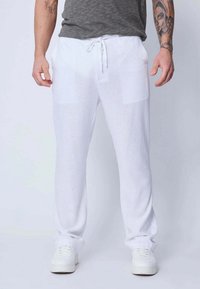 Pantalons en lin blancs avec taille élastique, deux poches avant et coupe ample, associés à des baskets blanches et une chemise grise.