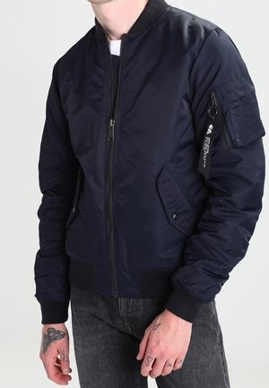 Marineblaues Bomberjacke mit einem Frontreißverschluss, gerippten Bündchen, zwei Seitentaschen und einer Reißverschlusstasche am Arm. Hergestellt aus glattem, glänzendem Stoff.