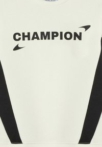 Biała bluza z czarnymi panelami bocznymi, z wyrazem "CHAMPION" w grubych czarnych literach oraz czarnym akcentem logo. Miękka tekstura.