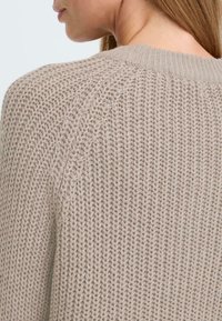 Lys beige strikket genser med et teksturert mønster, ribbestrikket detalj ved halsen, og en avslappet passform med senkede skuldre.