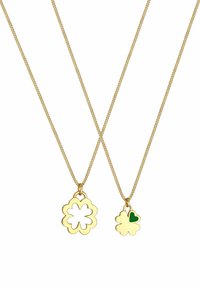 Goldfarbene Halsketten mit zwei Anhängern: der eine in Form einer hohlen Blume, der andere eine solide Blume mit einem grünen Herzakzent.