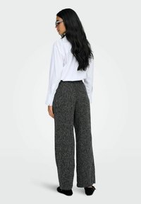 Pantaloni a gamba larga in tessuto nero e grigio abbinati a una camicia bianca con colletto, caratterizzati da una vestibilità rilassata e una vita elastica.
