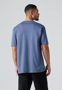 Korte ærmer, blå bomulds t-shirt med en afslappet pasform, rund halsudskæring og sømløse skuldre. Glat tekstur uden synlige mønstre.