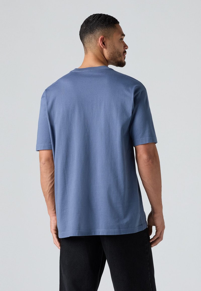 Camiseta de algodón azul de manga corta con un corte relajado, escote redondeado y hombros sin costura. Textura suave sin patrones visibles.