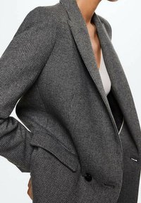 Šedý houndstooth blazer se strukturovaným designem, s vyklápěcími klopami a jedním knoflíkem. Obsahuje texturovanou látku a přední kapsy.