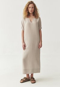 Beežist linasest kleit lühikeste, puffmade varrukatega ja V-kaelusega, ulatudes keskmise säärteni. Selga on pandud pruunid, nupukesega sandaalid. Lihtne ja elegantne kujundus.